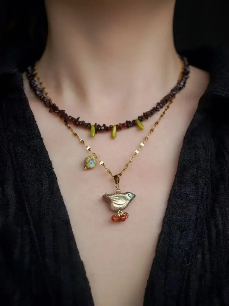 Garnet necklace with glass bird pendant on steel-titanium chain, inspired by the Thornbird story, part of Jewea' vintage handmade earrings and jewelry collection