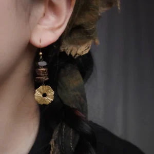 Close-up of a model wearing handmade "Wooden Branch" earrings featuring stacked coconut wood blocks and a pleated brass pendant, styled with a headscarf.