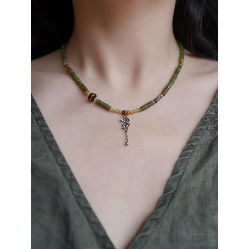 Jewea handmade silver jade necklace with natural tiger’s eye and a Thai silver leaf pendant, worn by a model in a green linen dress.