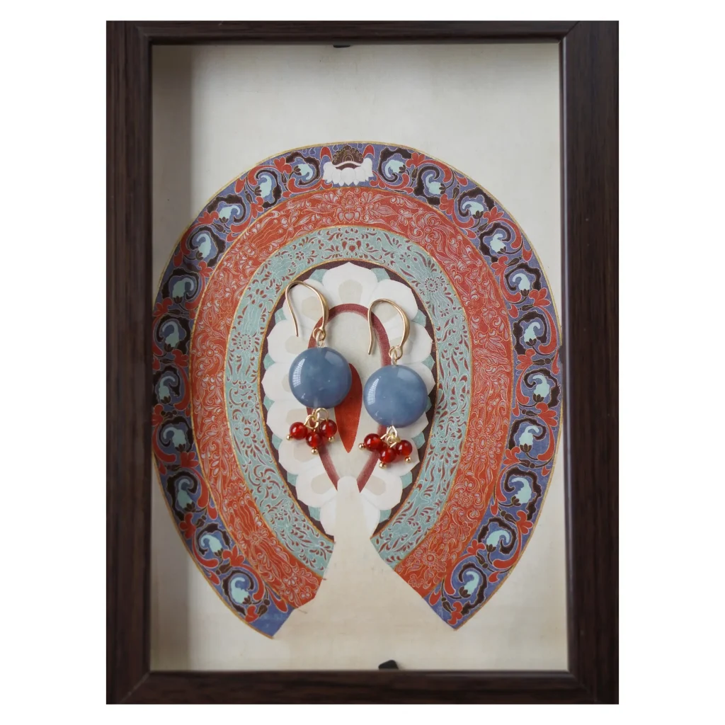Handmade Dunhuang-inspired earrings featuring round blue chalcedony stones with red agate bead clusters, displayed against a traditional mural-style background in a dark wooden frame.