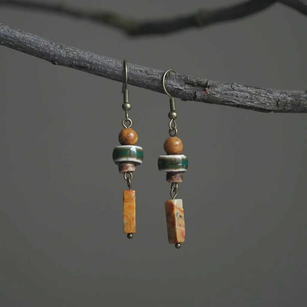 A handcrafted pair of ceramic and natural stone earrings featuring kiln-fired ceramic beads with deep earth-toned glaze and raw mineral stone accents, photographed against a soft neutral background.