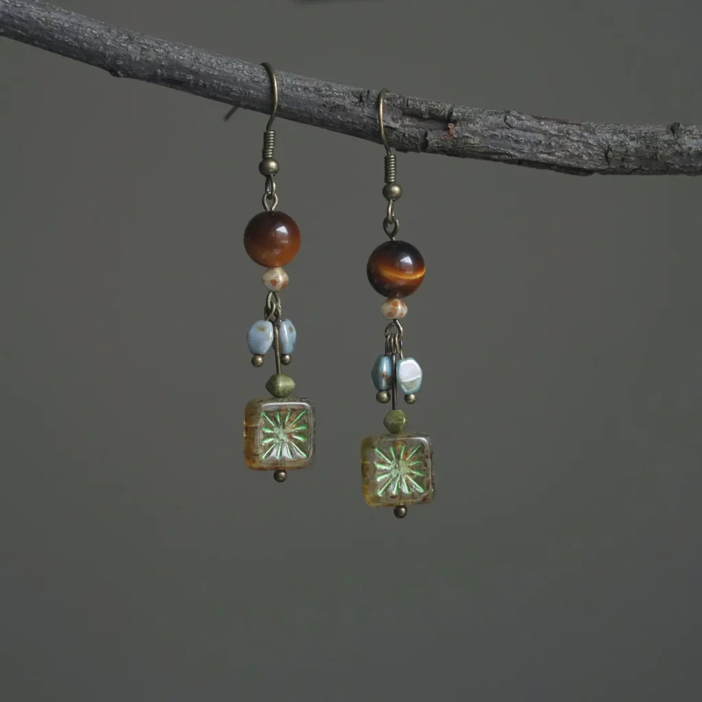 Vintage Tiger’s Eye drop earrings with star-patterned Czech glass beads, hanging on a rustic tree branch.