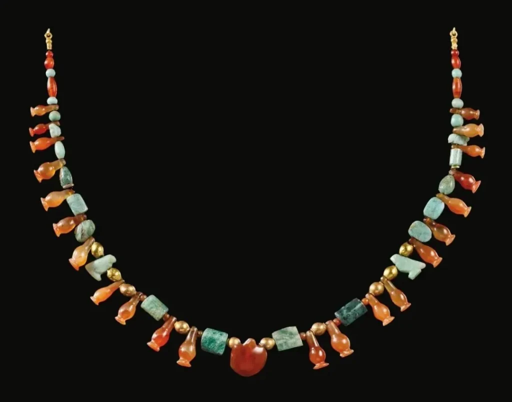 Illustration of an ancient Egyptian charm necklace featuring agate turtle, daisy pendant, Horus falcons, and scarabs, symbolizing protection and good fortune.