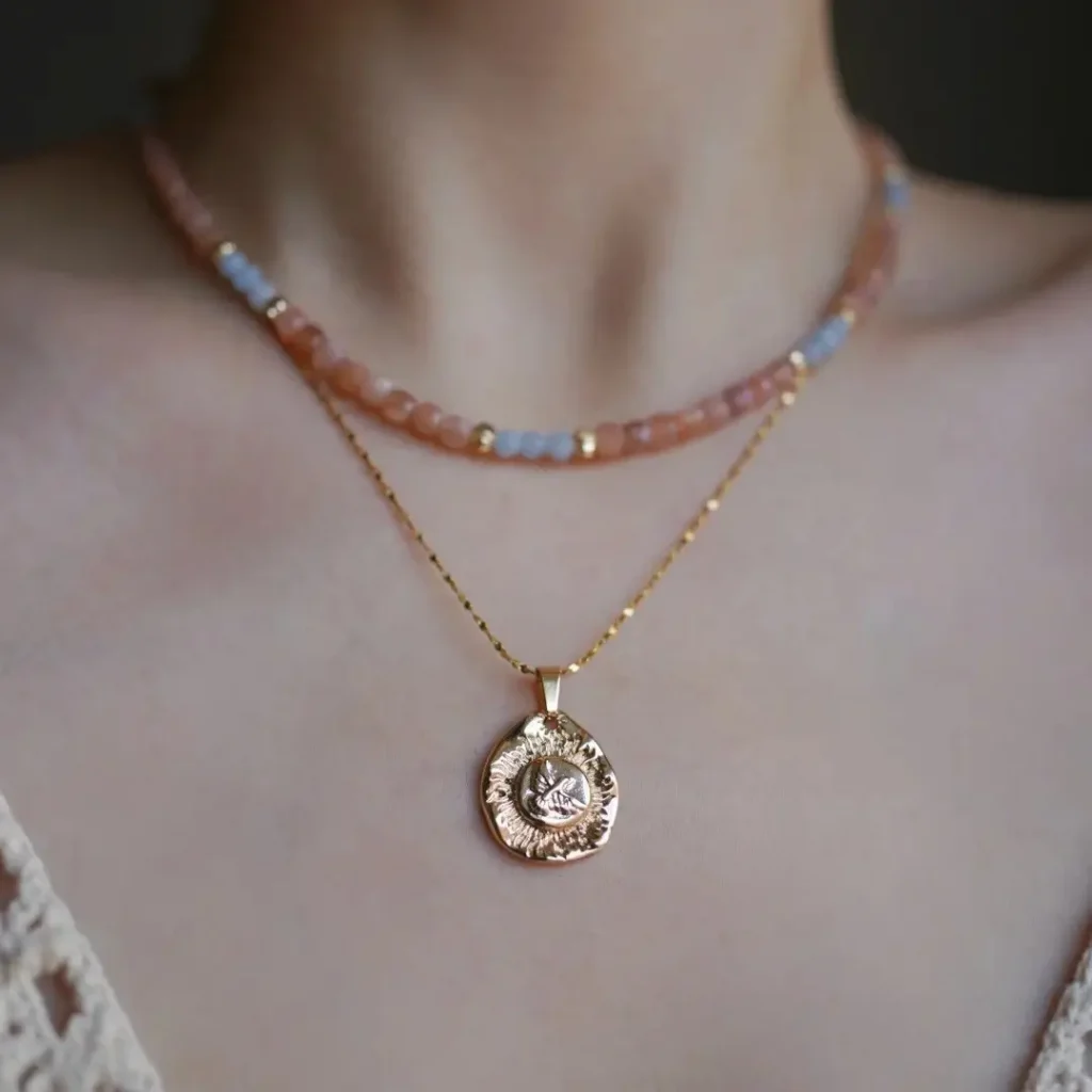 A model wearing a layered necklace with orange beads and a round gold bird relief pendant.
