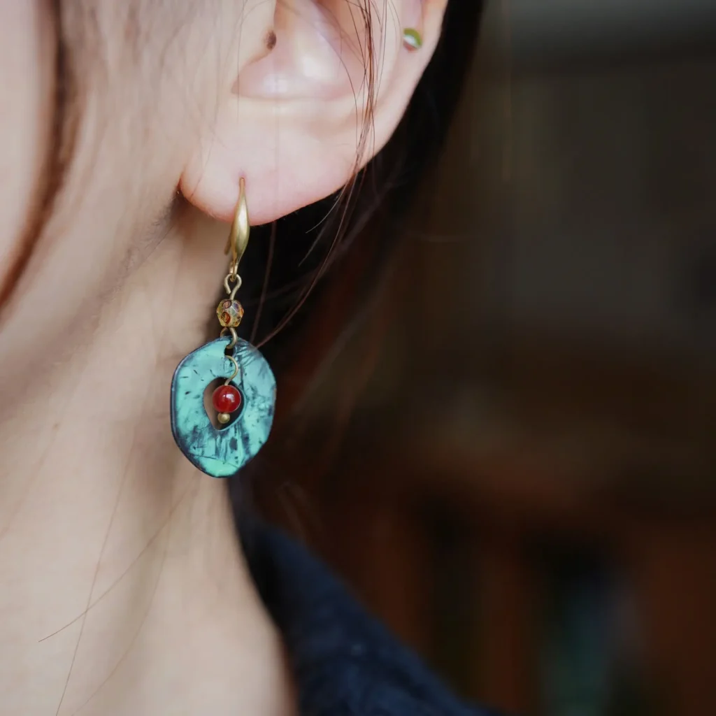 Close-up of a model wearing a handmade round oxidized brass earring with a red agate stone and greenish patina finish.