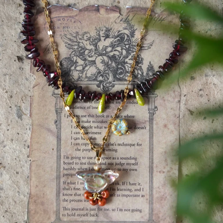 Layered thorn bird pendant necklace with vintage garnet beaded necklace on neutral background
