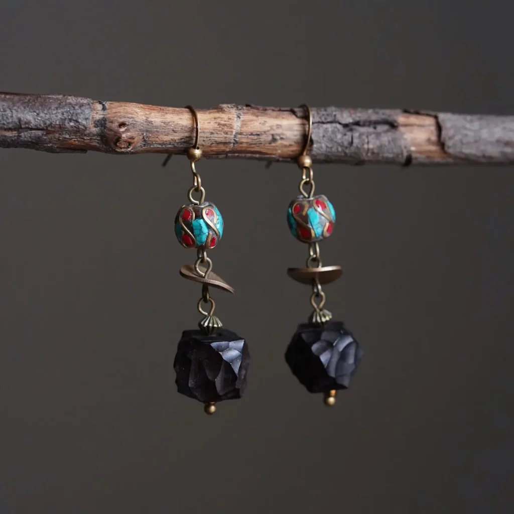 Vintage Tibetan dangle earrings made of hand-faceted ebony wood, brass, and inlaid turquoise and red agate fragments, hanging from a natural tree branch.