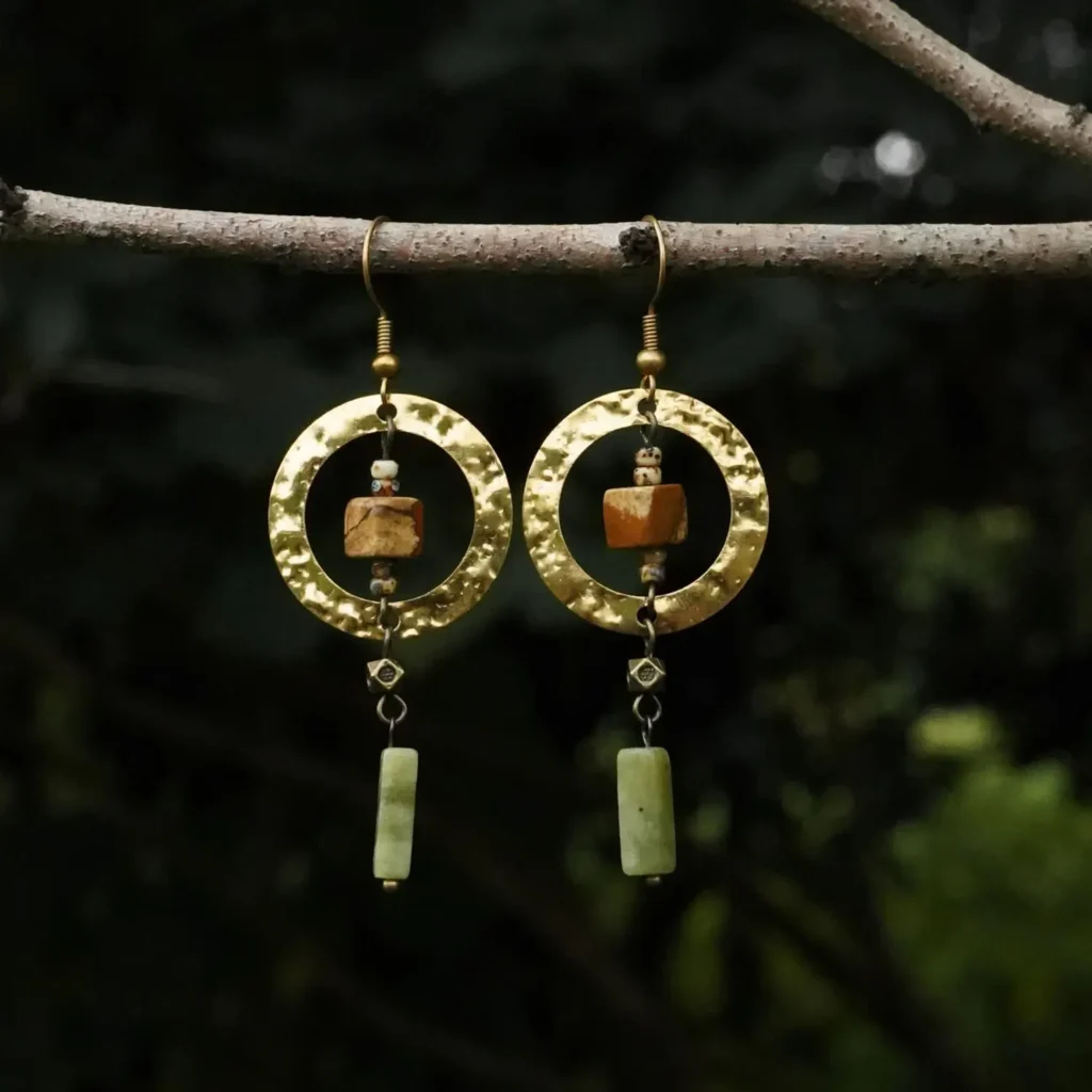 Moon Creek hammered hoop earrings with Southern Jade and picture stone dangles, suspended from a tree branch against a blurred forest background.