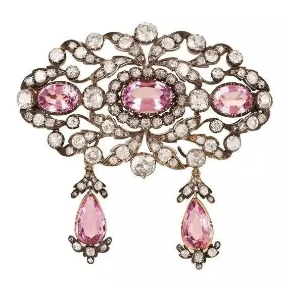 A stunning 1860 Victorian-era pendant and brooch featuring a large pink topaz stone set in a detailed filigree design, a classic example of jewelry from the period.