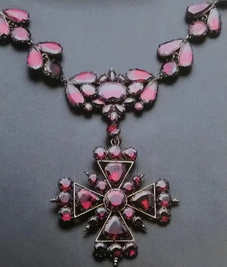 A vintage handmade gold necklace from the early 19th century, featuring stylized leaf-shaped garnet links and a detachable Maltese cross brooch and pendant, showcasing intricate craftsmanship and design.