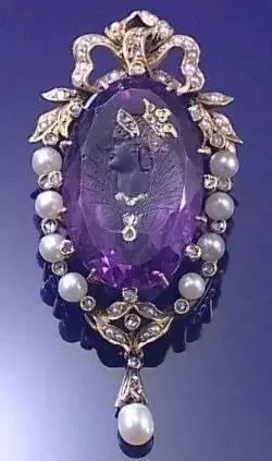 A purple amethyst pendant brooch carved with a portrait of Queen Victoria, accented with pearls and diamonds.
