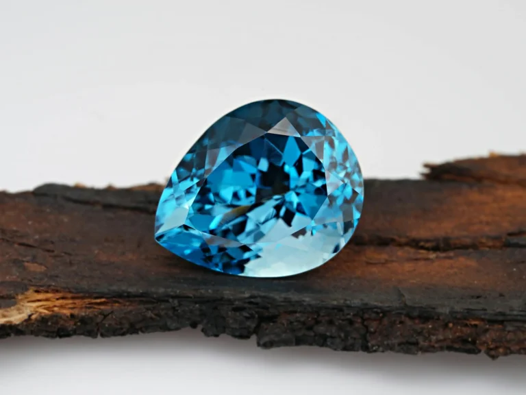 A stunning close-up of a faceted blue topaz gemstone, showcasing its crystal clarity as it rests on a piece of rustic wood.