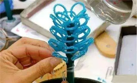 A wax tree inside a metal flask, with liquid plaster being poured in to create the casting mold.