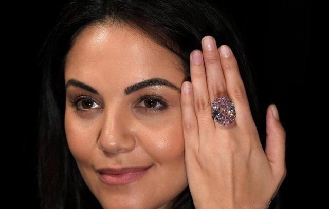 A celebrity wearing a pink diamond ring in a candid real-life photo, showing how fancy colored diamonds appear less vivid than in auction images.