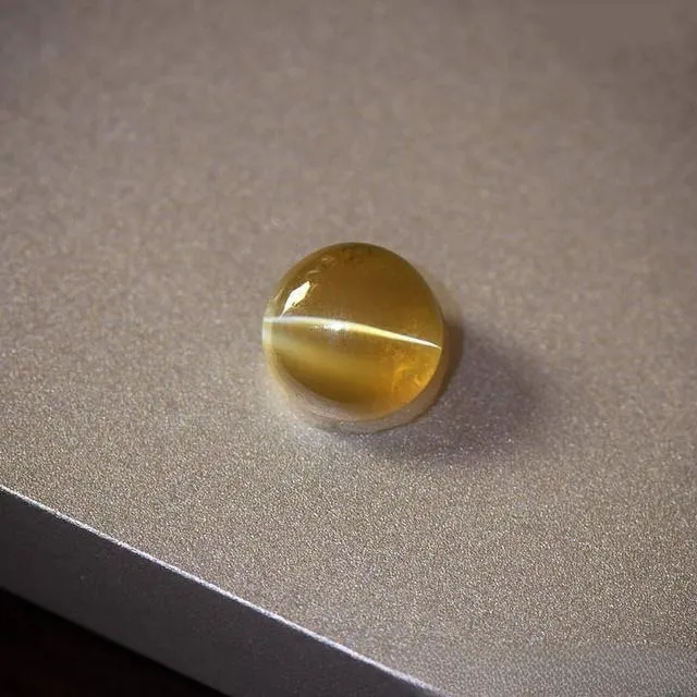 An image of a chrysoberyl cat's eye gemstone. The gem is typically cut into a cabochon shape, featuring a bright, straight cat's eye light band that moves with the light, with a clear crystal and a brilliant luster.