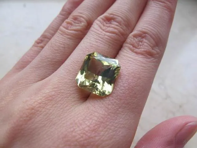 An image of a loose chrysoberyl gemstone placed on the back of a hand. The gem, with its golden-yellow or yellowish-green color and bright luster, is shown on the hand, which provides a sense of scale and allows viewers to appreciate its size and texture.