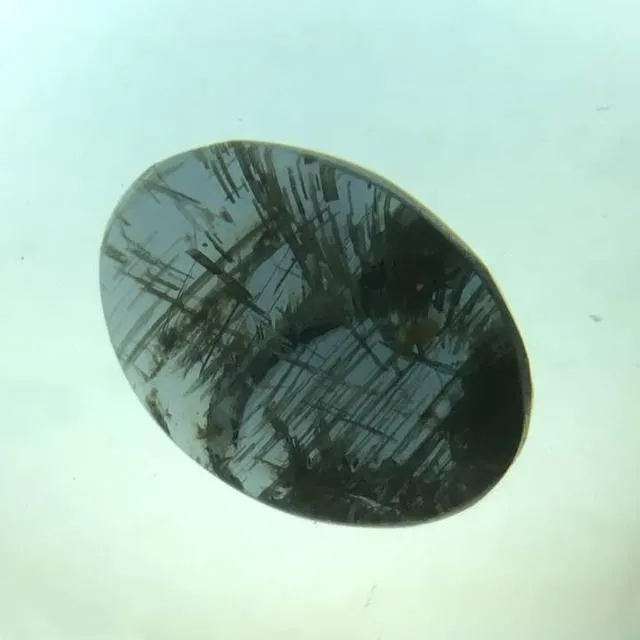 An image of a chrysoberyl crystal or loose gem with needle-like inclusions. Numerous fine, parallel needle-like inclusions are visible inside the gem, which are responsible for the cat's eye effect.