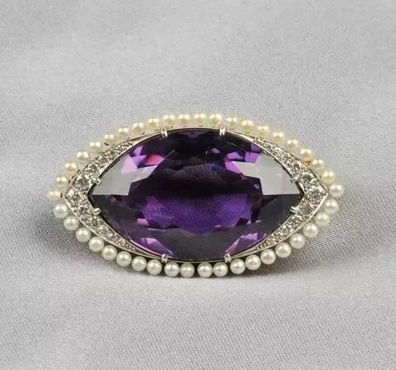 An eye-shaped ornament featuring a purple amethyst and pearls.