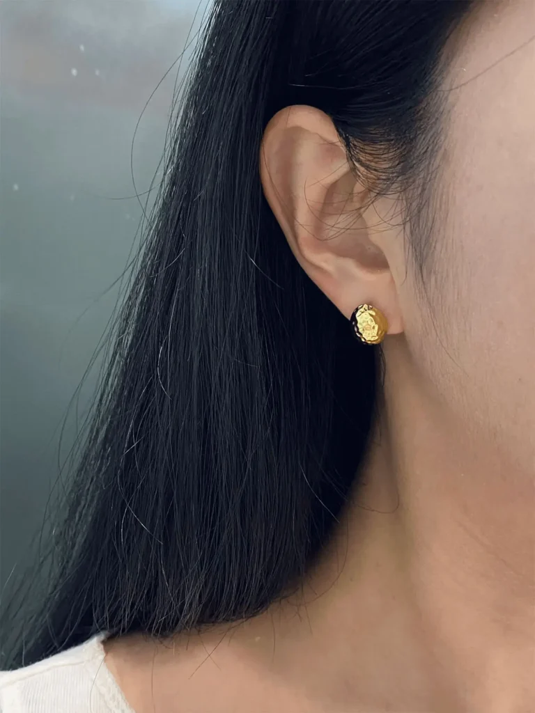 A woman wears gold-plated earrings with a curved design that fits naturally against the earlobe.