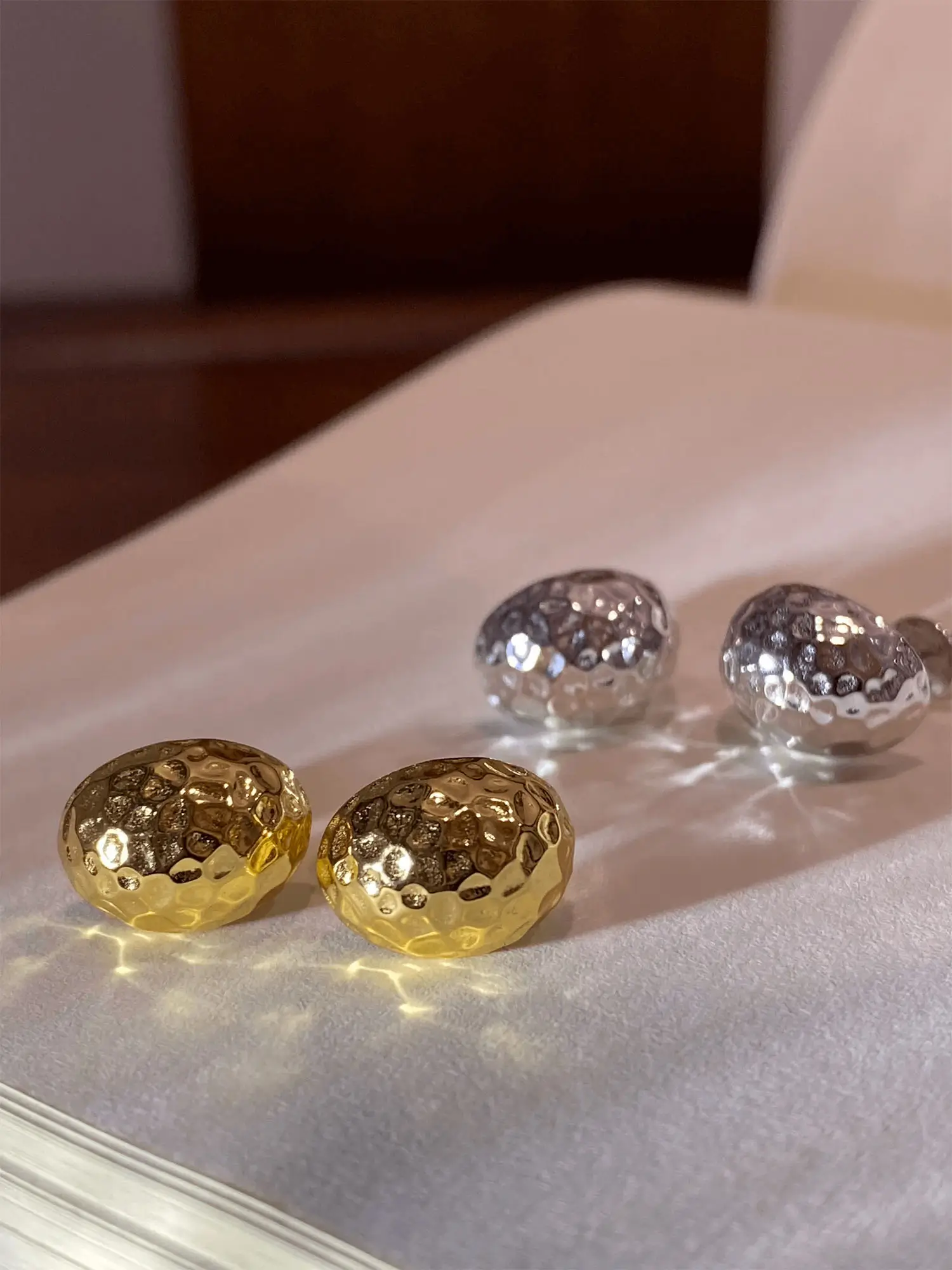 Two pairs of gold and silver sterling silver stud earrings with hand-hammered facets that reflect radiant light.