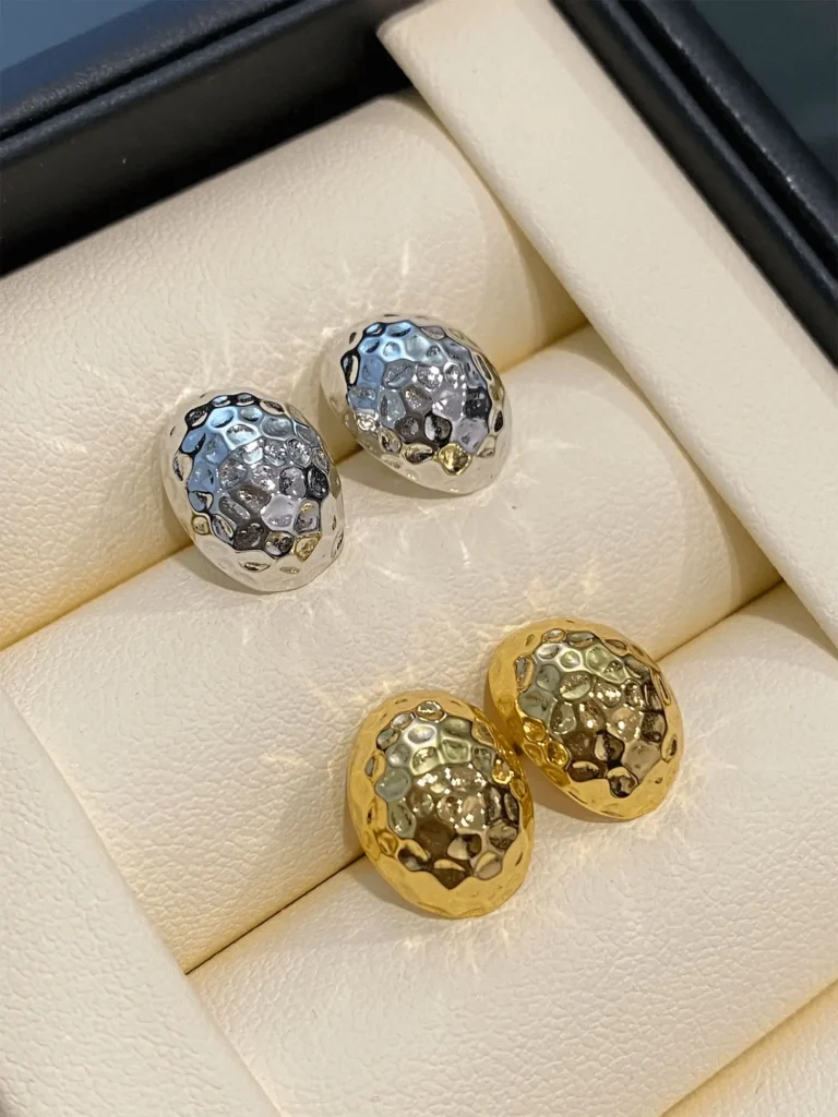 Handcrafted gold and silver earrings with curved surface displayed in a jewelry box under soft lighting.