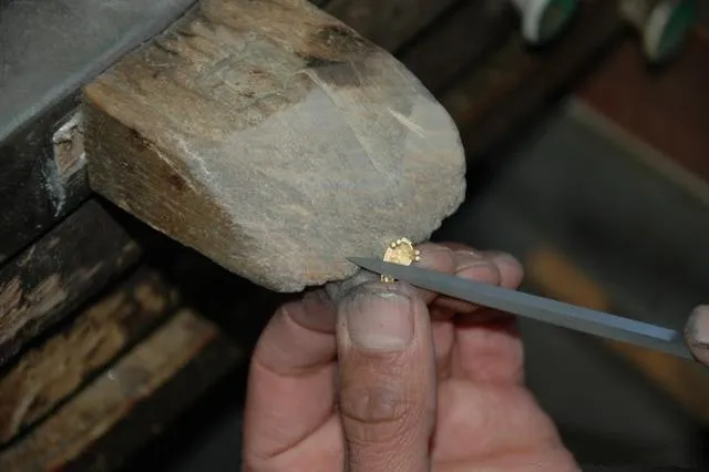 A jeweler using specialized tools to hand-shape and refine the surface of a metal jewelry casting.