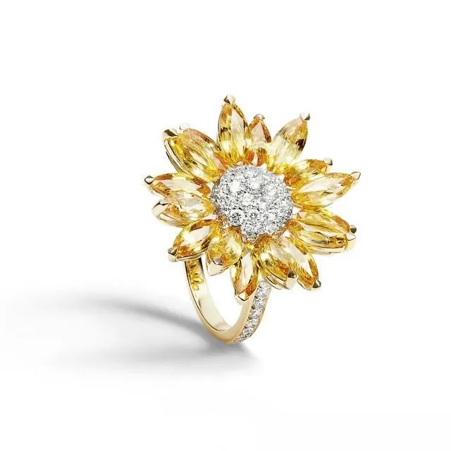An illustration of a luxury style gold diamond ring. The ring's main design features a floral motif, with petals formed by multiple marquise-cut yellow sapphires. A large center diamond is set within the petals, creating a brilliant and creative design with striking color contrast.