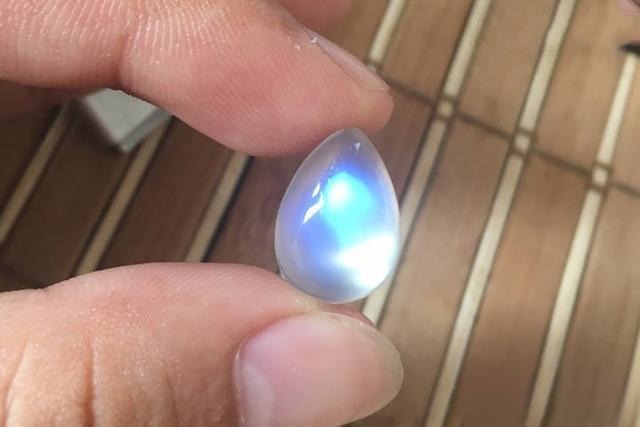Drop-shaped moonstone photographed in natural light, showing the blue adularescence on its surface.