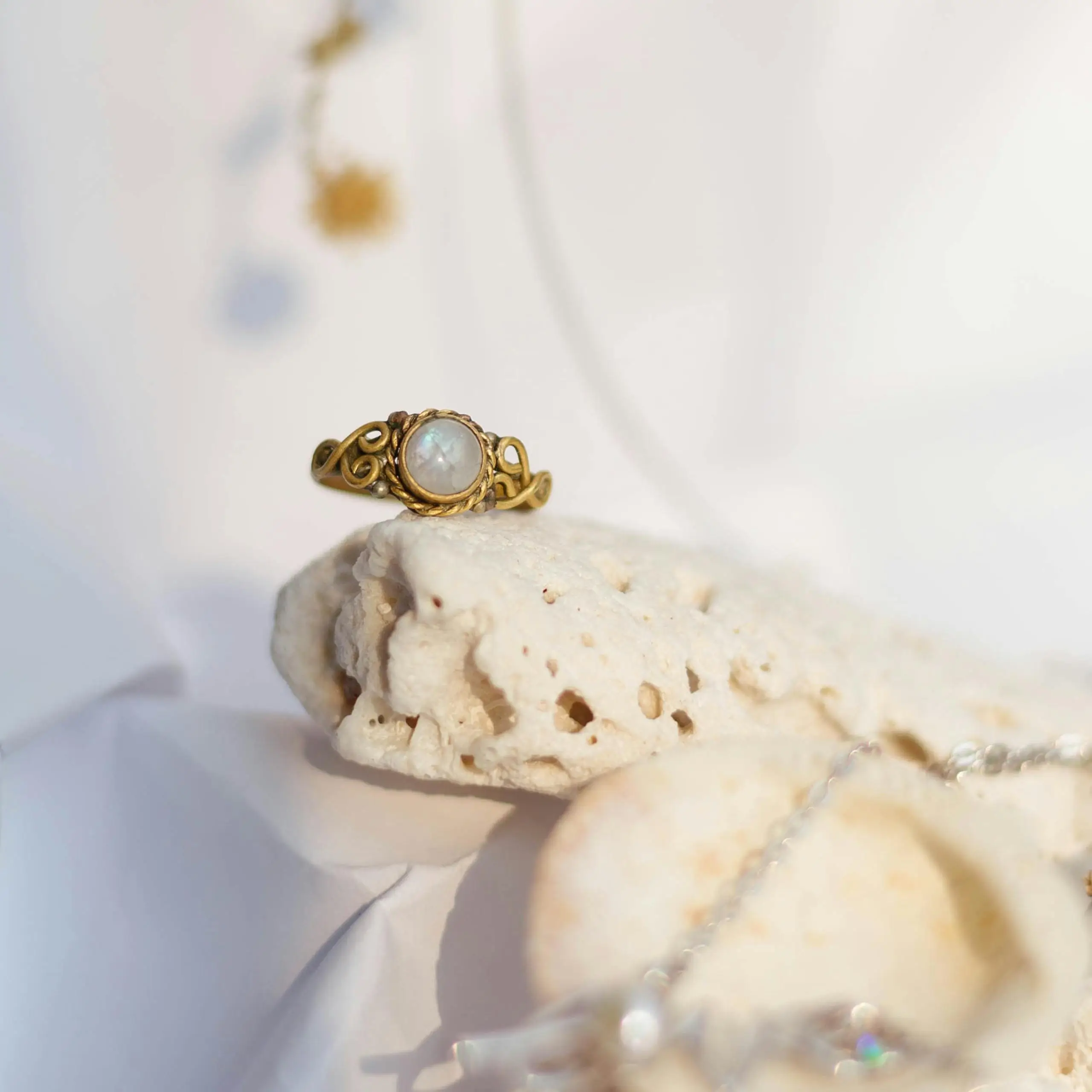 Close-up of a gold ring with a moonstone, highlighting its blue adularescence on a natural stone background.