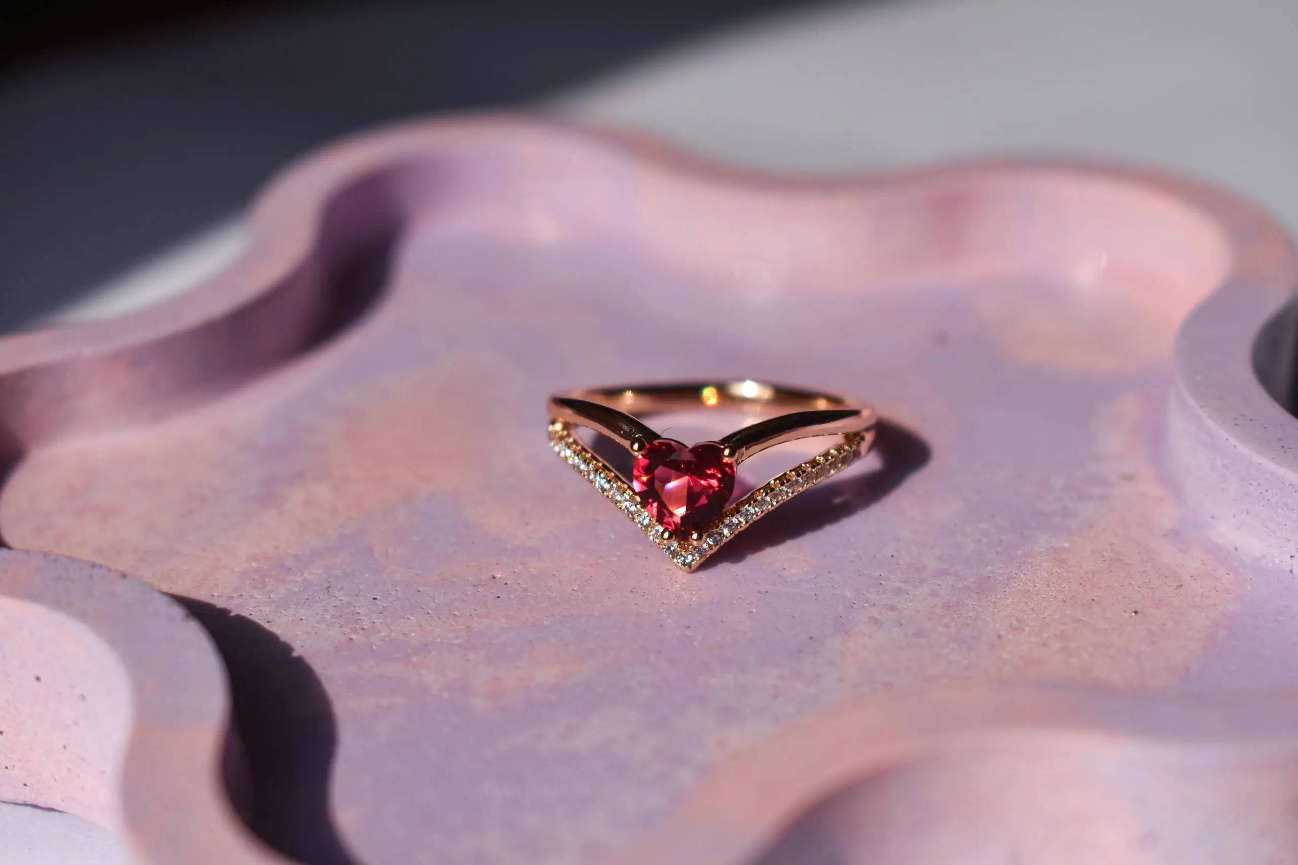 Heart-shaped fancy colored diamond ring on a pink decorative tray, illustrating why pink and green diamonds are highly valued.