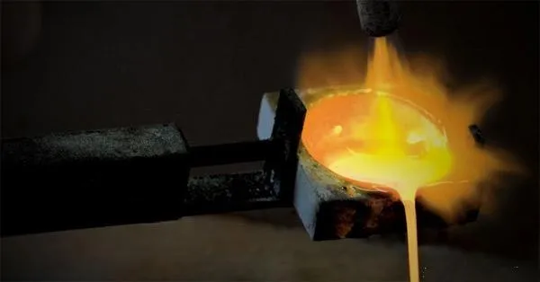 Molten gold being poured from a crucible into a plaster mold during the jewelry casting process.
