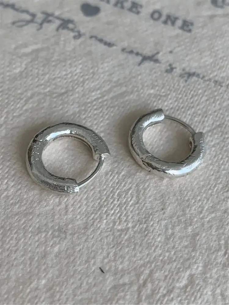 Small silver hoops displayed to show minimalist design, lightweight feel, and handcrafted details.
