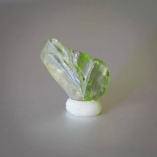 An image of a V-shaped chrysoberyl crystal specimen. The crystal has a distinctive V-shape and a yellowish-green color. This twinning habit is known as a knee-shaped twin in gemology.