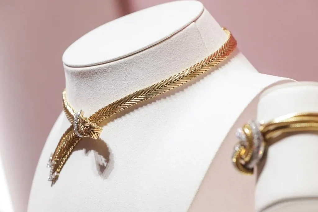 An illustration of a luxurious Van Cleef & Arpels necklace from the 1950s. The piece features a sophisticated and intricate design, possibly with floral or nature-inspired motifs, crafted from gold or platinum and adorned with precious gems, reflecting the elegant style of the mid-20th century.