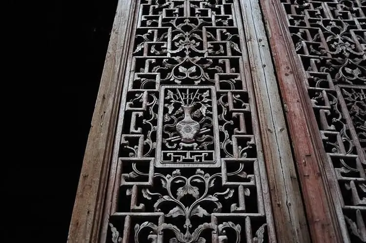 An image of a hollow-carved wooden door decoration featuring a vase with three halberds. The intricate carving, which is a common motif in traditional Chinese architecture, symbolizes a wish for a peaceful promotion in official rank.