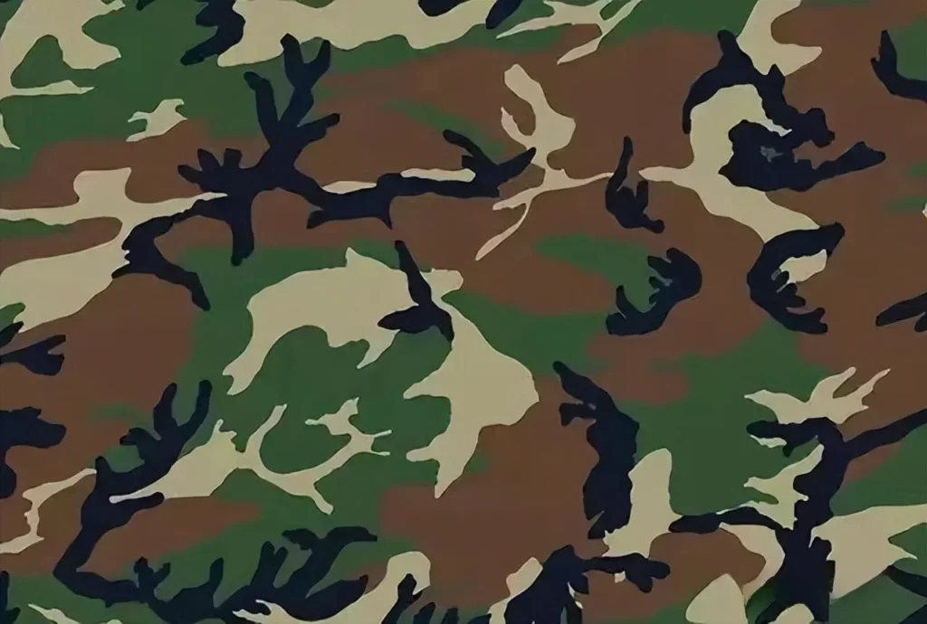 An illustration of a woodland camouflage pattern. The design consists of irregular shapes in shades of green, brown, black, and tan, intended to mimic a forest and jungle environment.