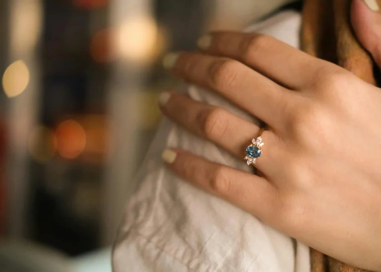 Close-up of a hand wearing a sapphire engagement ring surrounded by diamonds, symbolizing the elegance and rarity of September birthstone pieces.
