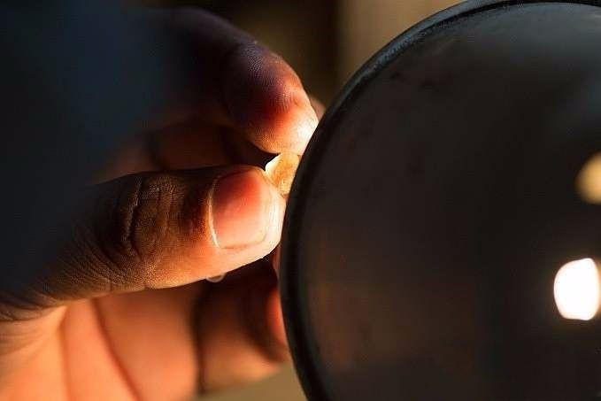 Gemstone cutter studying the rough stone at the faceting machine, determining the table orientation and final cutting method