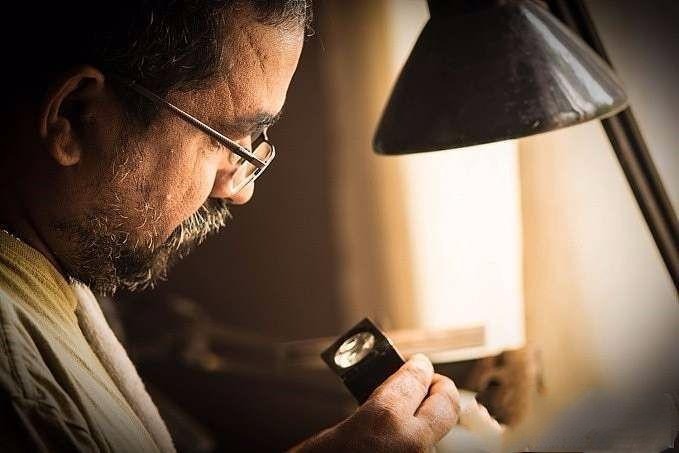 Experienced gemstone cutter at workbench with long beard and calm demeanor, exuding wisdom and serenity while performing gemstone cutting.