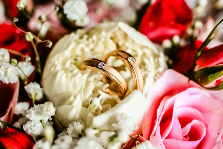 Close-up of gold wedding rings nestled in colorful rose petals, symbolizing love and marriage