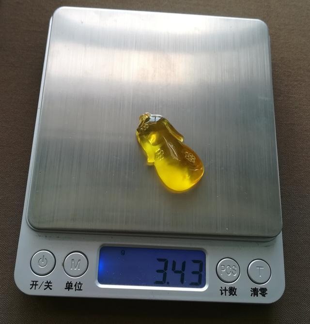 Jewea custom golden beewax qipao displayed on a digital scale, highlighting the exquisite craftsmanship and weight of the gemstone-inspired design.