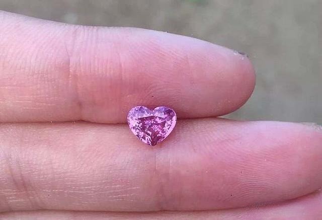 Hand holding a heart-shaped Madagascar pink sapphire, naturally unheated, showing purple-gray tones due to high blue content
