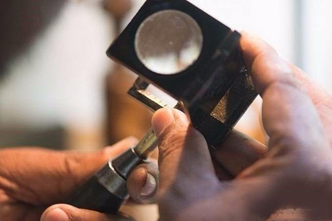 Using a magnifying glass to check the gemstone's bottom point alignment and ensure all facets are on the same level
