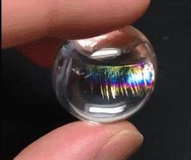 Quartz crystal showing rainbow lash inclusions from one angle, with light creating delicate, shimmering eyelash-like patterns