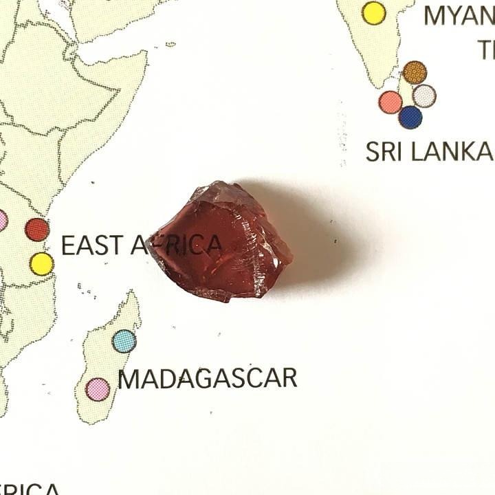 A ruby rough with a large table and shallow depth, illustrating uneven proportions common in natural gemstones.