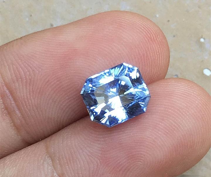 Hand holding a 5.58-carat finished Sri Lankan gemstone cut from an original 11-carat rough, slightly lighter in color but radiantly brilliant.