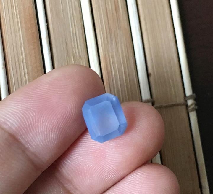 Hand holding a 7-carat preformed Sri Lankan gemstone, shaped from an original 11-carat rough to reveal its clarity and color.