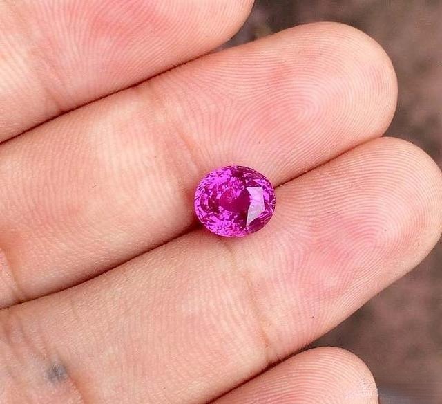 Hand holding a Sri Lankan pink sapphire showing vivid, nearly "fiery" pink color, highly transparent and typically unheated