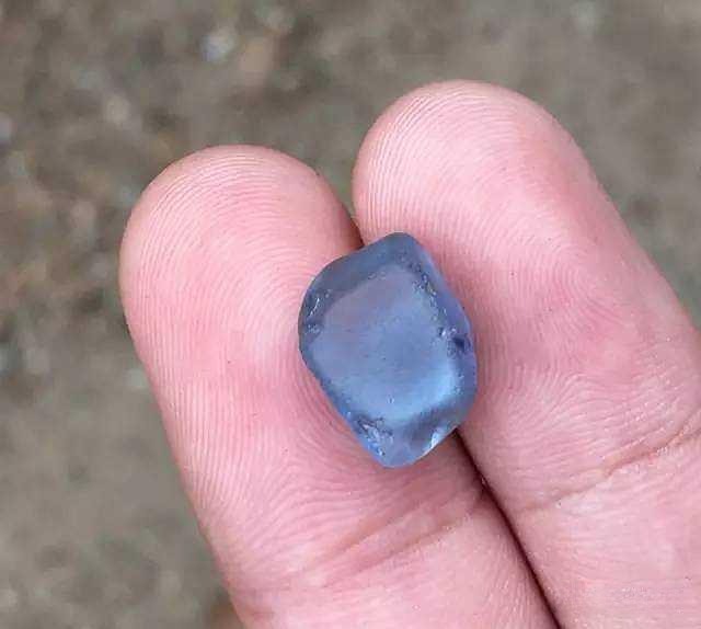 Hand holding a 11-carat natural untreated rough gemstone from Sri Lanka, showing its raw clarity and color.