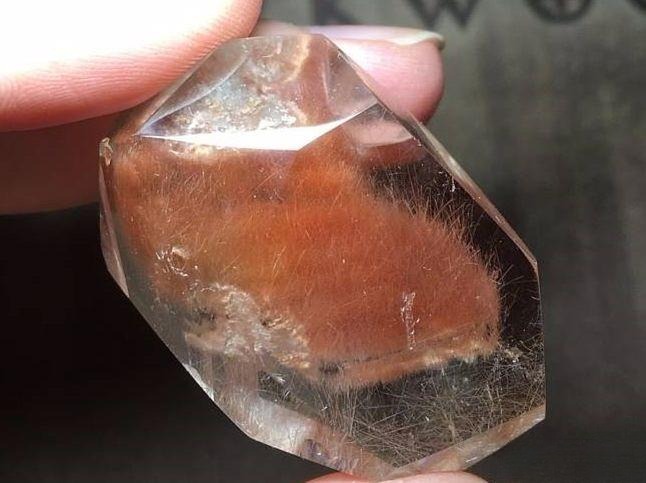 Handheld Venus quartz with red rabbit hair inclusions showing fine rutile fibers floating inside like delicate hairs in water